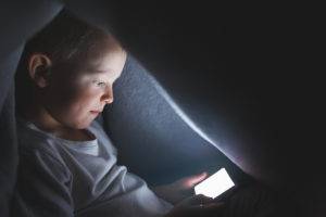 Niño bajo las sábanas jugando con un smartphone